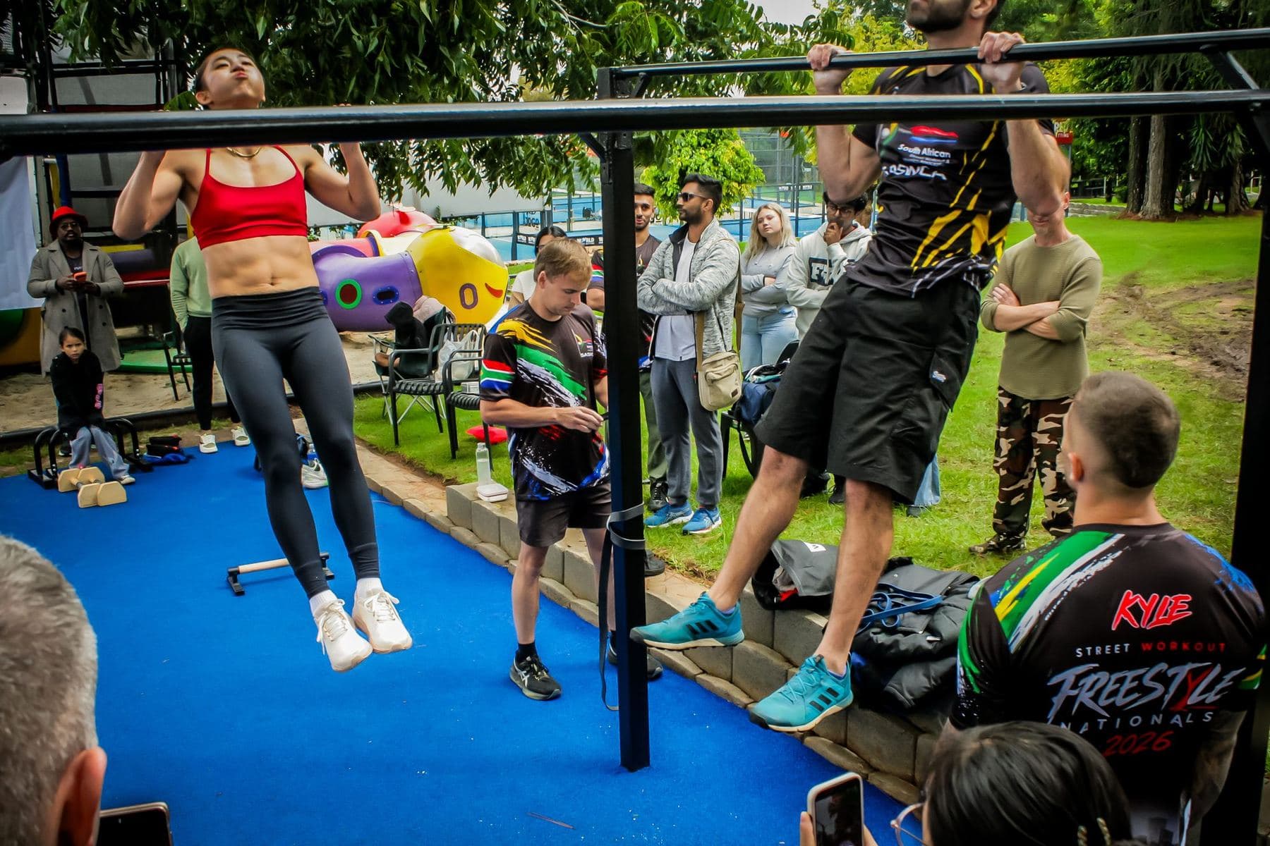 Competitors mid-repetition on the pull-up bars at Endurance Nationals, judges and spectators alongside.