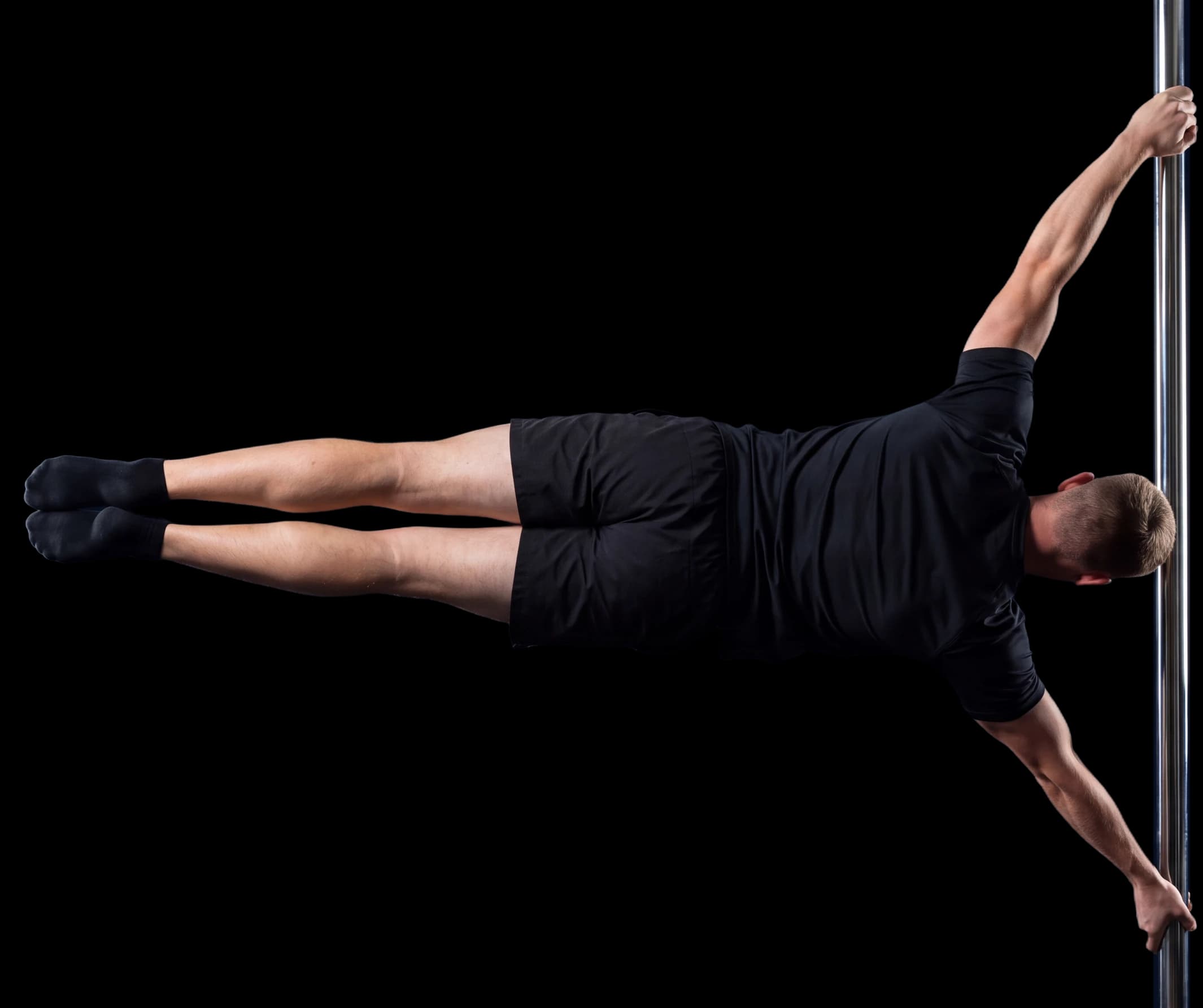 An athlete in black training kit holding a straight-arm human flag on a chrome pole, body level with the ground.